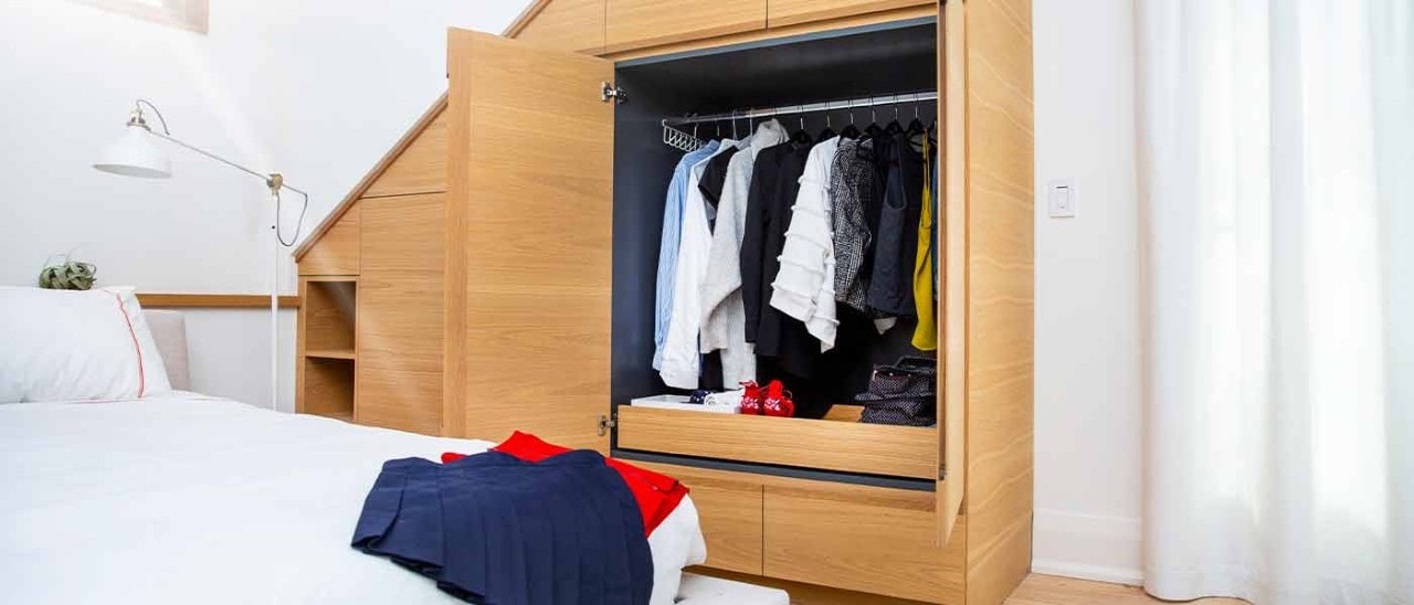 A bedroom with a small closet open and clothes on the bed.